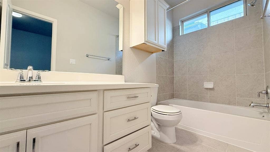 2937 Mossy Springs Drive, Leander, TX 78641 Bathroom featuring a white vanity with drawers and cabinets, a large wall-mounted mirror, a tub-shower combination with tile surround, and an upper wall cabinet