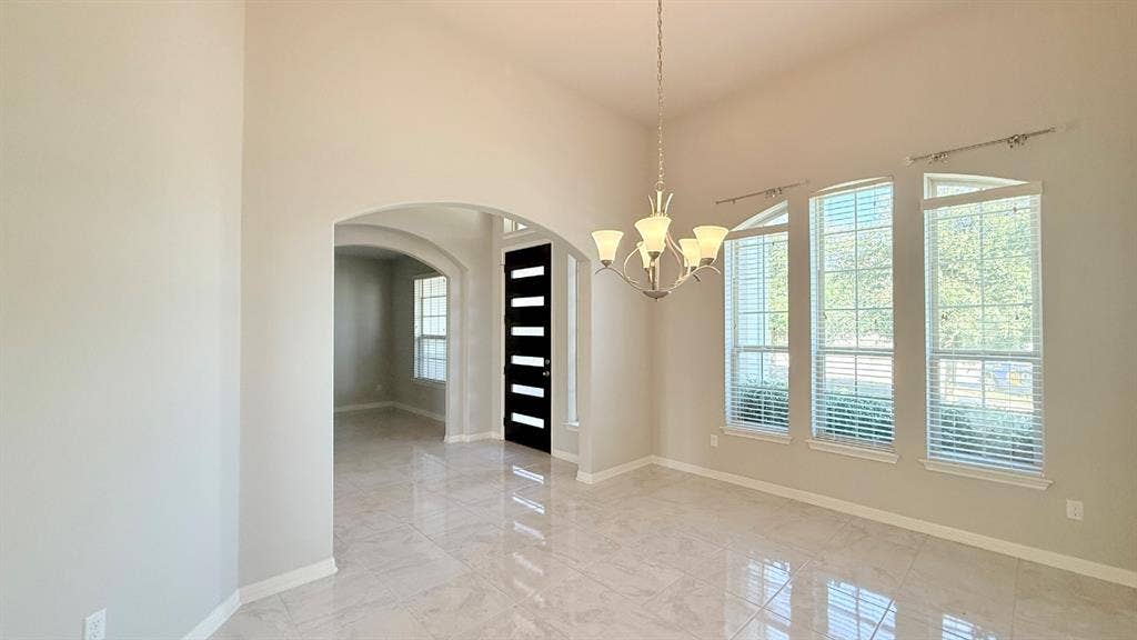 2937 Mossy Springs Drive, Leander, TX 78641 High ceilings featuring an arched entryway, polished stone-finish tile flooring, a multi-arm chandelier, and tall windows with horizontal blinds