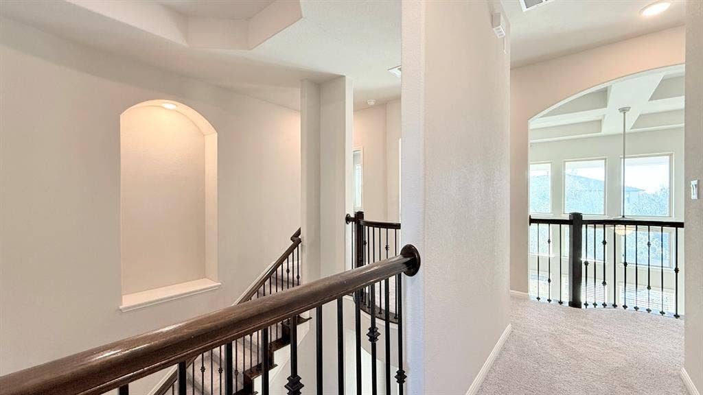 2937 Mossy Springs Drive, Leander, TX 78641 Stairway featuring an arched wall niche, wrought-iron balusters, and a wooden handrail, leading to a landing with a coffered ceiling and arched entryway