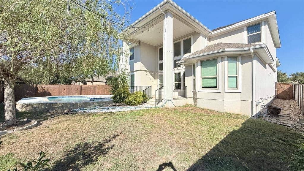 2937 Mossy Springs Drive, Leander, TX 78641 Two-story exterior featuring a light-toned facade, an elevated covered rear porch with a prominent column, multi-pane windows, and a backyard swimming pool enclosed by wooden fencing
