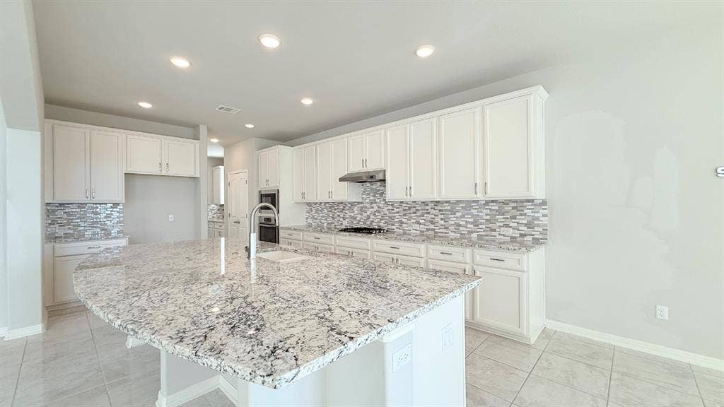 2937 Mossy Springs Drive, Leander, TX 78641 Kitchen featuring a large center island with stone countertop, white cabinetry, integrated stainless steel appliances, multi-tonal backsplash, and recessed lighting