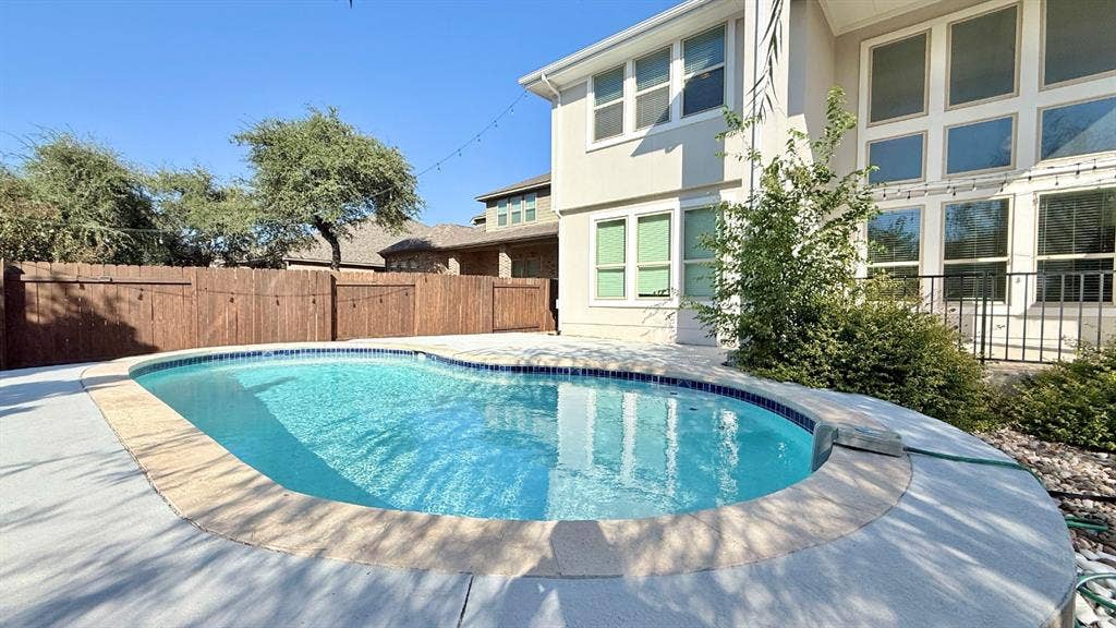 2937 Mossy Springs Drive, Leander, TX 78641 Backyard pool with concrete decking, perimeter wood fencing, and multi-story exterior with large windows