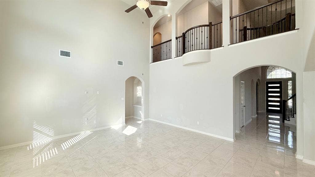 2937 Mossy Springs Drive, Leander, TX 78641 Double-height ceiling, polished tile flooring, wrought iron staircase railing, arched architectural detailing, and integrated ceiling fan
