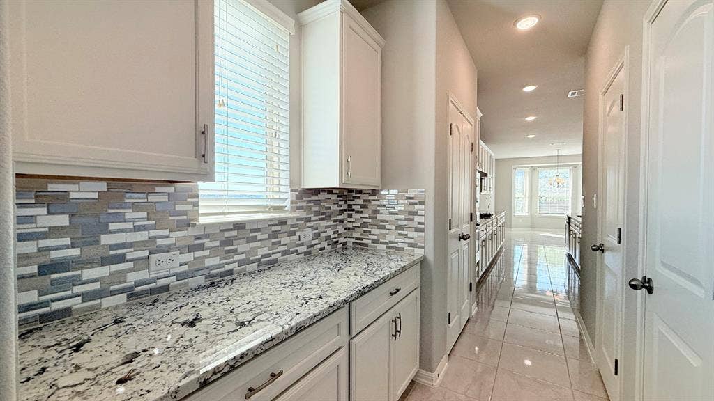 2937 Mossy Springs Drive, Leander, TX 78641 White cabinetry, stone-surface countertops, multi-tonal rectangular tile backsplash, and polished tile flooring