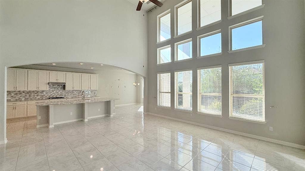 2937 Mossy Springs Drive, Leander, TX 78641 High-ceiling living area featuring a multi-level grid of large windows, tile flooring, arched architectural detailing, and a kitchen island with stone-surface countertops