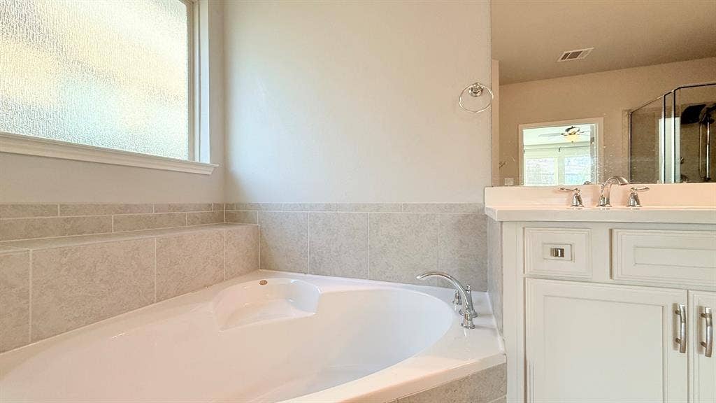 2937 Mossy Springs Drive, Leander, TX 78641 Corner soaking tub with tile surround, white cabinetry, integrated countertop, and chrome fixtures
