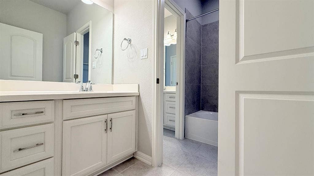 2937 Mossy Springs Drive, Leander, TX 78641 Bathroom featuring white shaker-style cabinetry, a solid surface countertop with an integrated basin, a large wall-mounted mirror, and a tub-shower combination with dark gray tiled surround