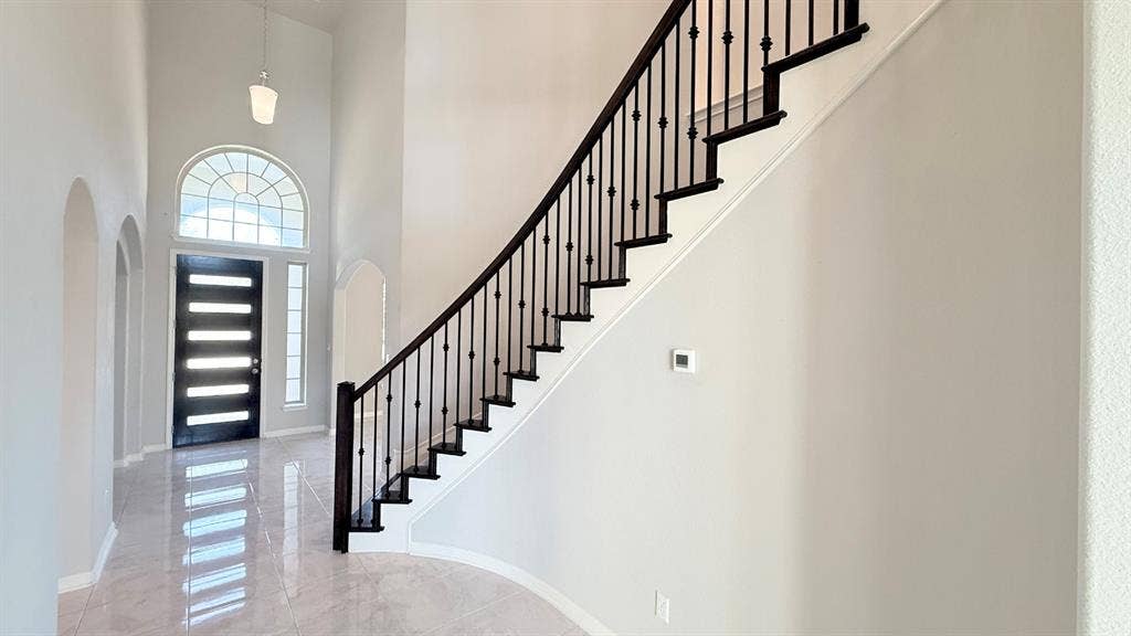2937 Mossy Springs Drive, Leander, TX 78641 Grand entryway featuring vaulted ceilings, polished tile flooring, a dark-toned front door with horizontal glass panels, a semi-circular transom window, and a staircase with decorative iron balusters