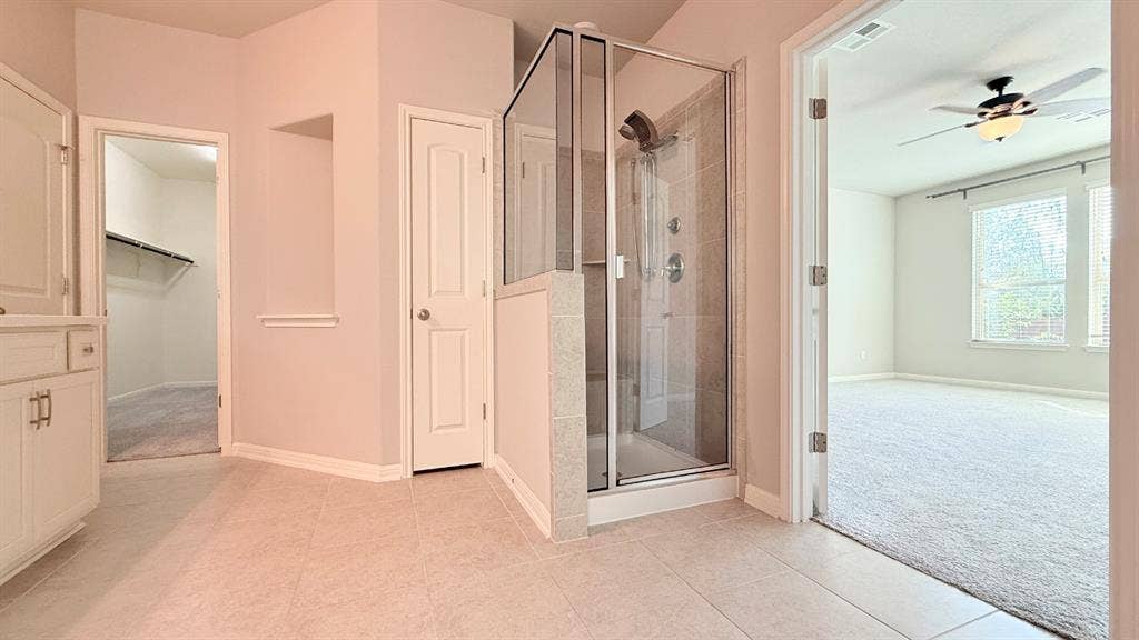 2937 Mossy Springs Drive, Leander, TX 78641 Shower enclosure with tiled surround and multi-head fixture, tile flooring, built-in cabinetry, and walk-in storage area