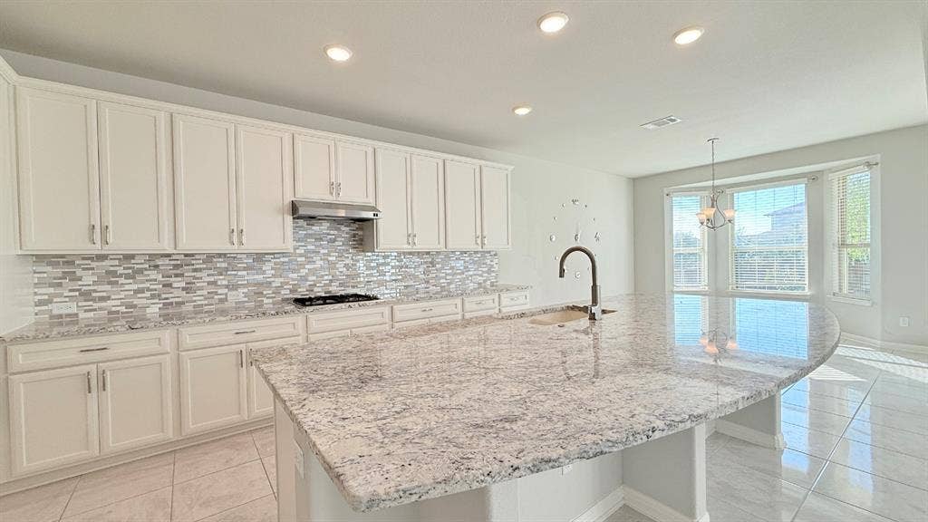2937 Mossy Springs Drive, Leander, TX 78641 Kitchen featuring white cabinetry, stone countertops, multi-toned tile backsplash, stainless steel range hood, and large central island