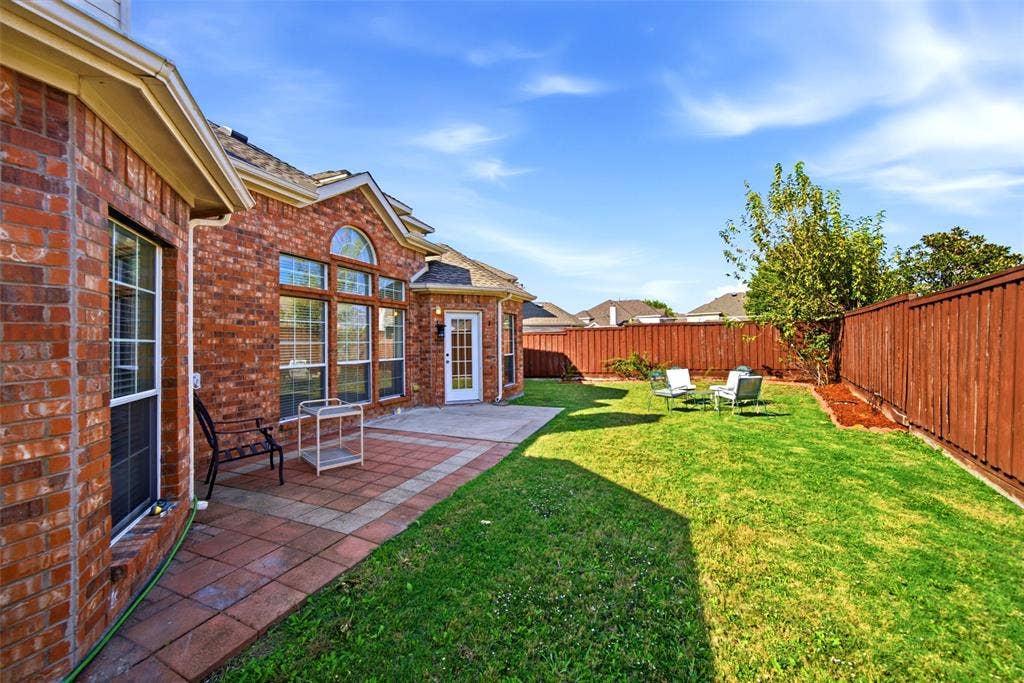 Rear exterior featuring red brick masonry, a tiled patio, arched window detailing, and a fenced backyard