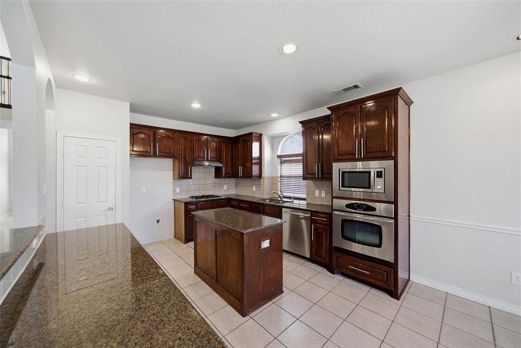 Kitchen featuring dark wood cabinetry, stone countertops, central island, tiled flooring, and built-in stainless steel appliances
