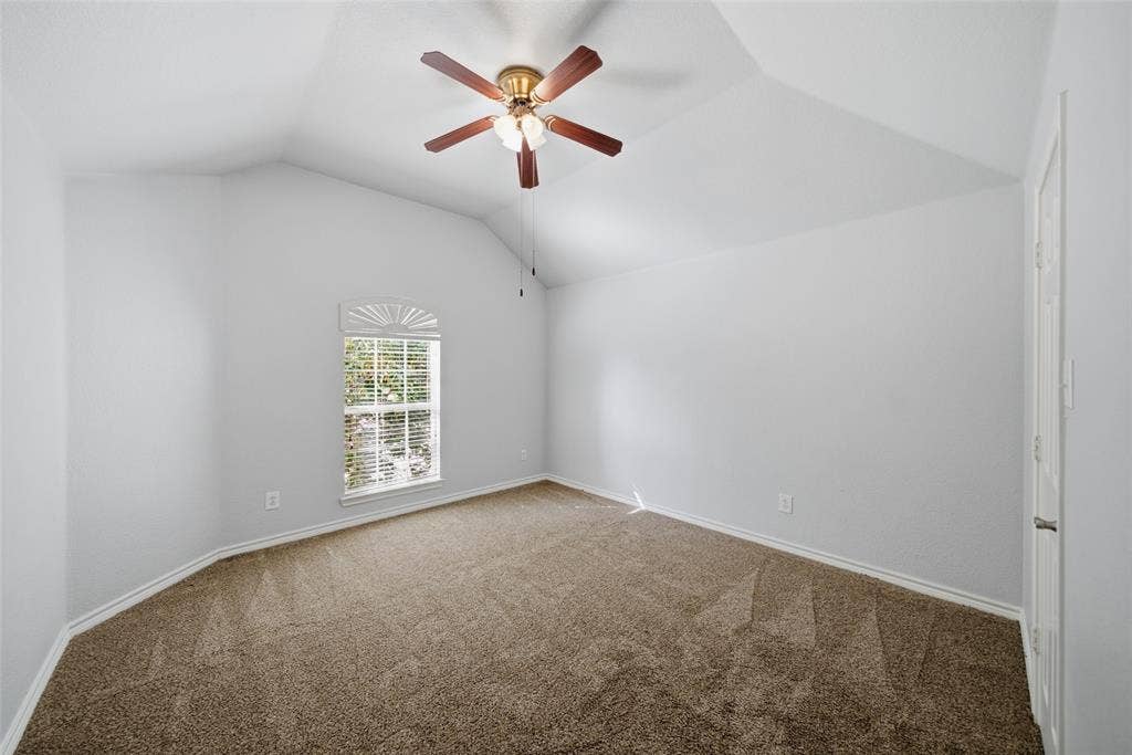 Vaulted ceiling with a central multi-blade ceiling fan, arched window, and neutral wall-to-wall carpeting