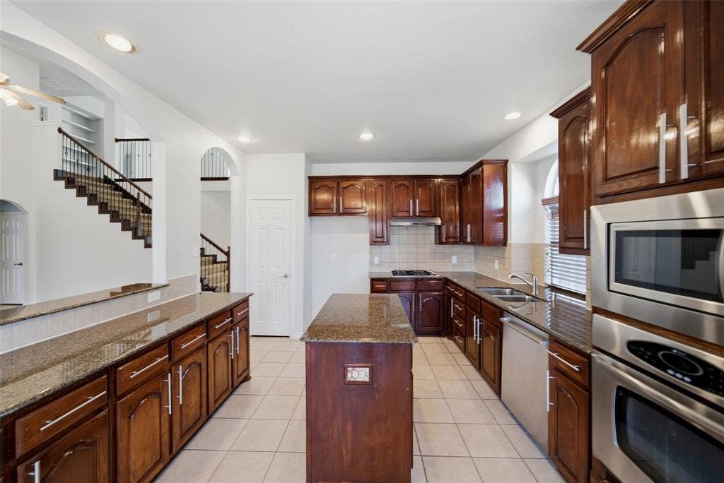 Kitchen featuring dark wood cabinetry, stone-surface countertops, central island, tile flooring, and integrated stainless steel appliances