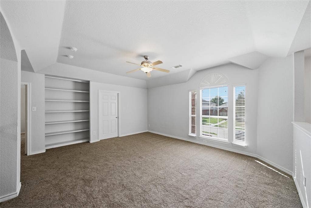 Tray ceiling, built-in recessed shelving, ceiling fan with integrated lighting, and multi-pane windows with arched detailing