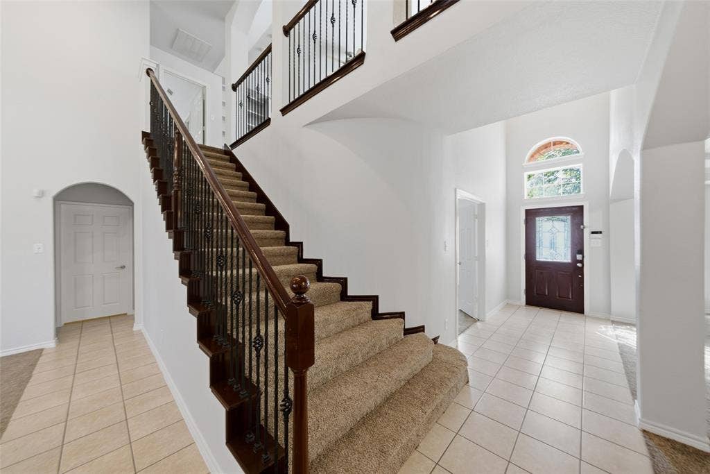 Entryway featuring high ceilings, arched architectural detailing, tile flooring, a staircase with a wooden handrail and iron balusters, and a front door with a decorative glass insert