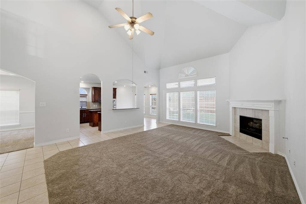 Vaulted ceiling living area featuring a fireplace with a decorative mantel, arched wall openings, multi-pane windows with a fanlight, and a central ceiling fan