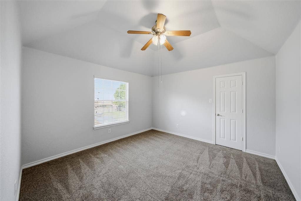 Vaulted ceiling featuring a ceiling fan with integrated lighting, neutral carpeting, and a multi-panel interior door