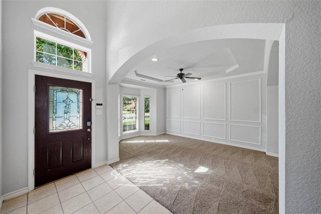 Entryway featuring a dark wood door with decorative glass inlay, arched transom window, high ceilings, custom wall molding, and a tray ceiling with a center fan