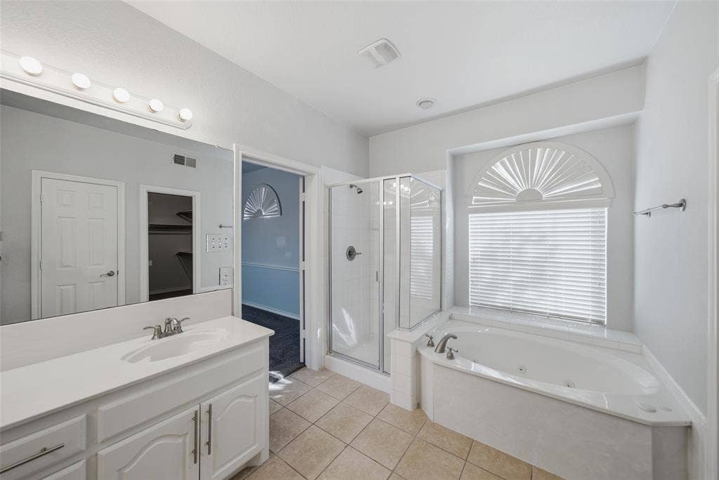 Bathroom featuring a dual-sink vanity with white cabinetry and solid-surface countertops, a glass-enclosed shower, a jetted soaking tub, and an arched window