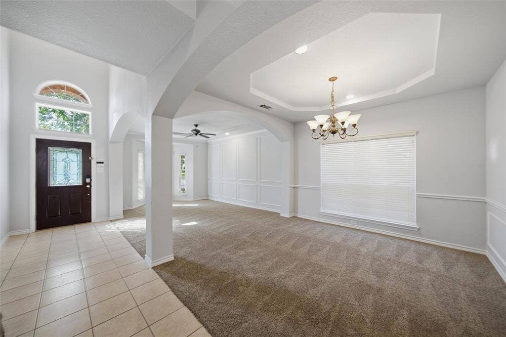 Entry featuring ceramic tile flooring, arched architectural detailing, tray ceiling with multi-arm chandelier, and decorative wall molding