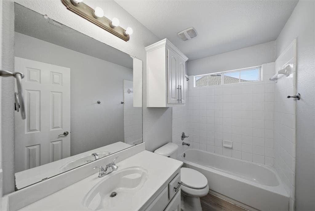 Bathroom featuring a vanity with an integrated sink, wall-mounted cabinetry, a full-width mirror, and a tub-shower combination with white tile surround