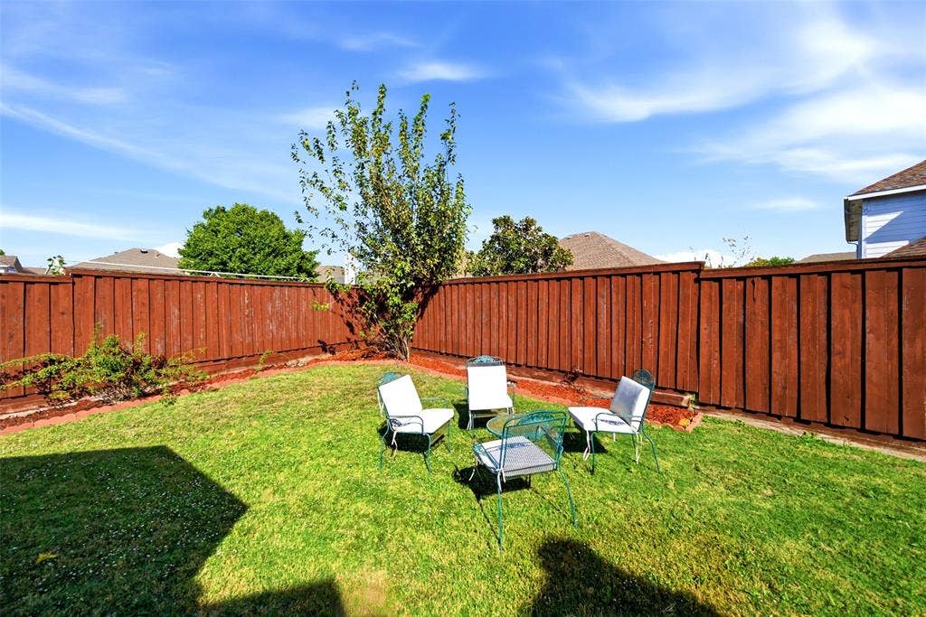 Backyard featuring a manicured lawn, perimeter wood fencing, and established trees