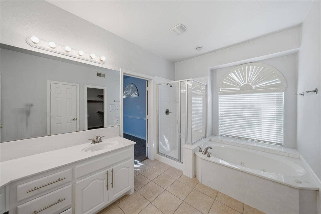 Bathroom featuring a dual-sink vanity with white cabinetry, a walk-in glass-enclosed shower, a jetted soaking tub, and an arched window with louvered shutters