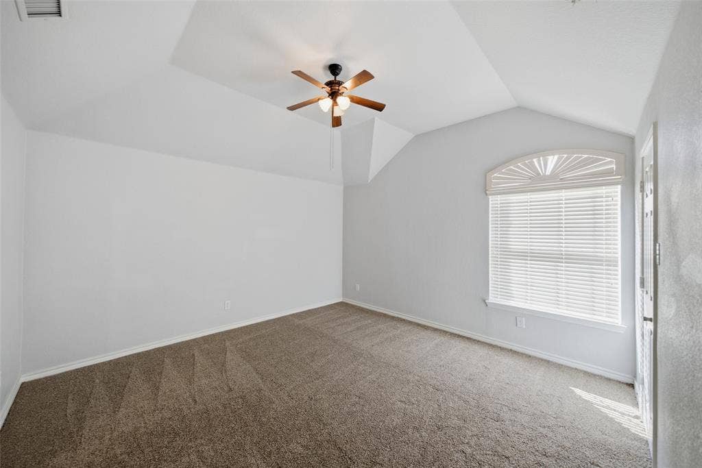 Vaulted ceiling featuring a central multi-blade ceiling fan, neutral carpeting, and a sunburst-arch window with horizontal blinds