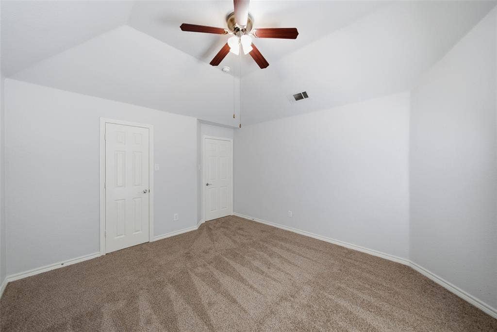 Vaulted ceiling featuring a central multi-blade ceiling fan with integrated light fixture, neutral wall finishes, and carpeted flooring