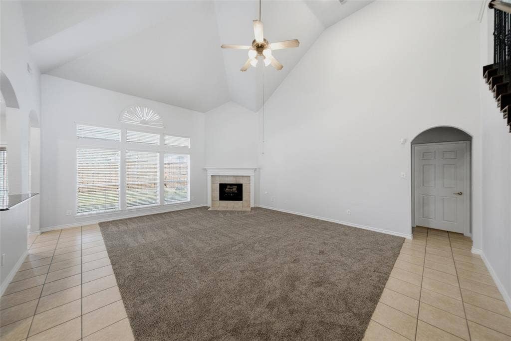 Vaulted ceilings, fireplace with tile surround, arched architectural details, ceramic tile flooring, and multi-pane windows with semi-circular transoms