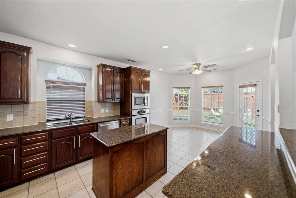Kitchen featuring dark wood cabinetry, stone countertops, an island, recessed lighting, and tile flooring