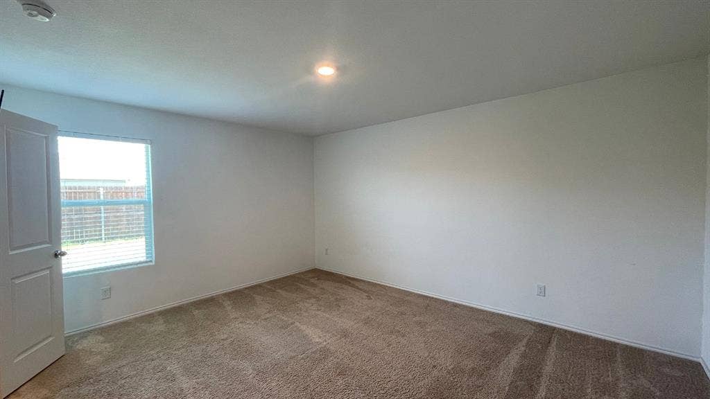 Neutral wall-to-wall carpeting, crisp white wall finishes, single-pane window, and a multi-panel interior door