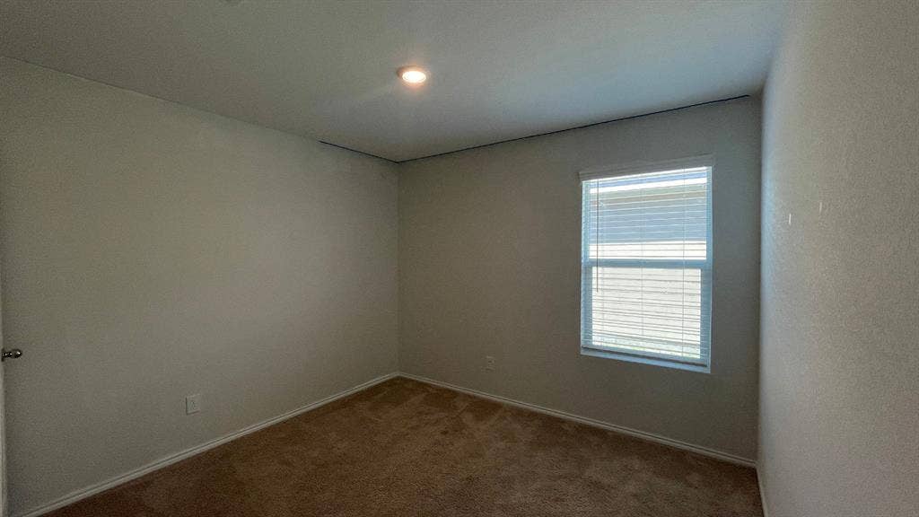 Neutral-toned interior space featuring wall-to-wall carpeting, a single-pane window with horizontal blinds, and a recessed ceiling light fixture