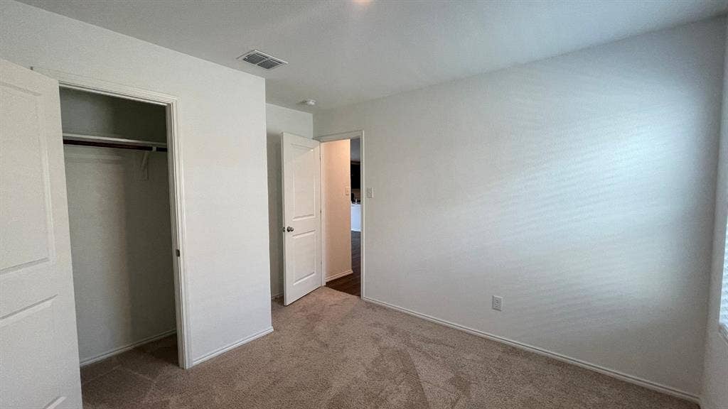 Neutral-toned wall paint, plush carpeting, multi-panel interior doors, and a built-in closet with overhead shelving