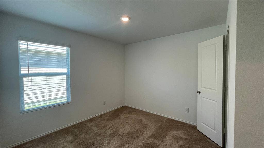 Neutral-toned wall paint, neutral carpeting, single-pane window with installed blinds, and a white interior door with a silver-finish knob
