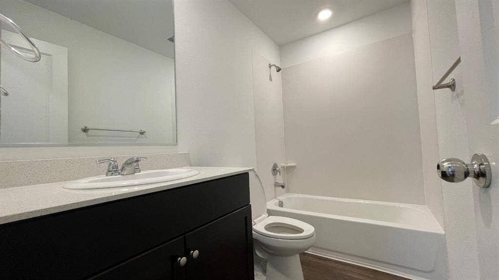 Bathroom featuring a dark wood-finish vanity, light-toned stone countertop with an undermount sink, recessed lighting, and a tub-shower combination with a surround
