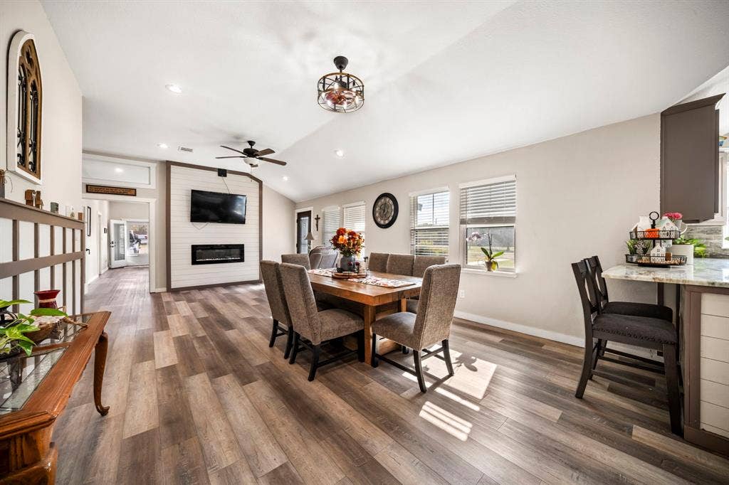 205 Newman Road, Ennis, TX 75119 Open-concept living space featuring wood-finish flooring, vaulted ceilings, recessed lighting, horizontal plank accent wall with integrated fireplace, and stone-surfaced kitchen island