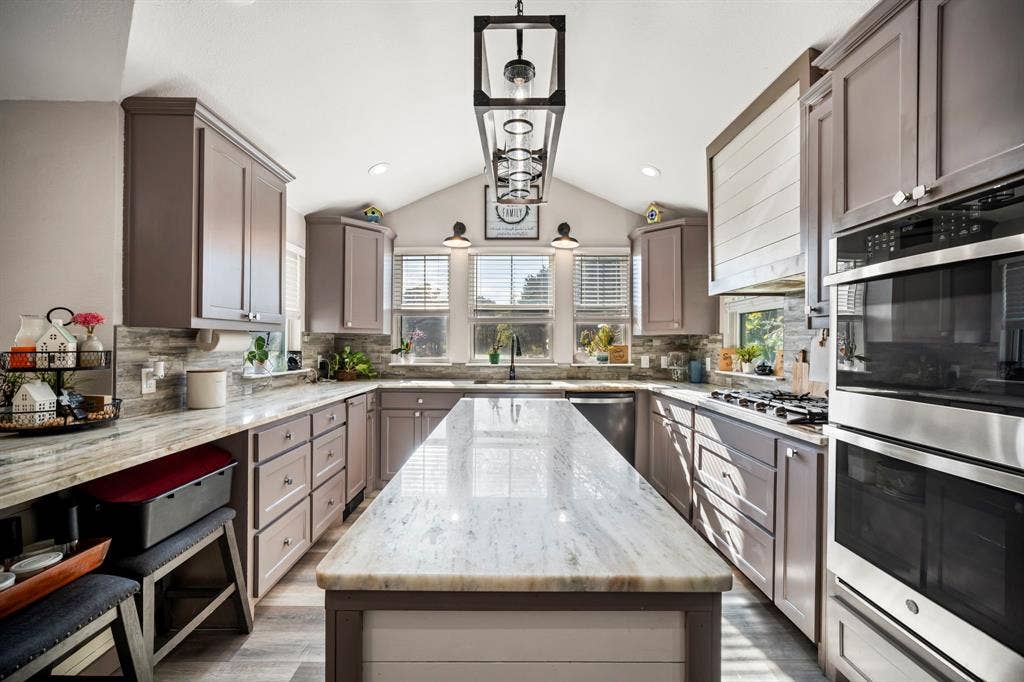 205 Newman Road, Ennis, TX 75119 Kitchen featuring custom cabinetry, expansive stone-surface island, vaulted ceiling, stainless steel double wall ovens, and geometric pendant lighting