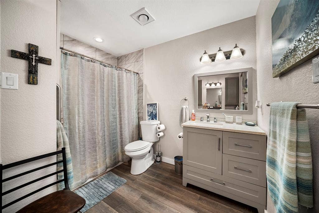 205 Newman Road, Ennis, TX 75119 Bathroom featuring a shaker-style vanity with stone-finish countertop, wood-finish flooring, three-light wall-mounted fixture, and tile-surround shower