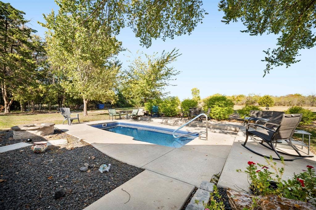 205 Newman Road, Ennis, TX 75119 Rectangular in-ground pool with concrete surround, stone fire pit, and mature trees