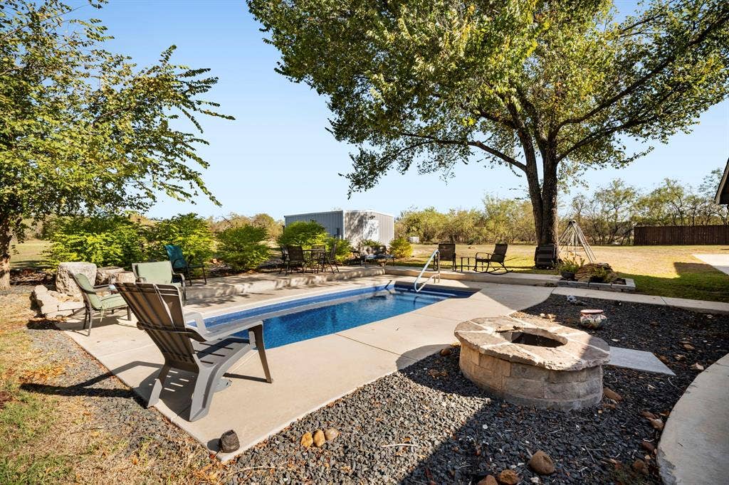 205 Newman Road, Ennis, TX 75119 Inground swimming pool with concrete decking, stone-surround fire pit, mature shade trees, and detached storage structure