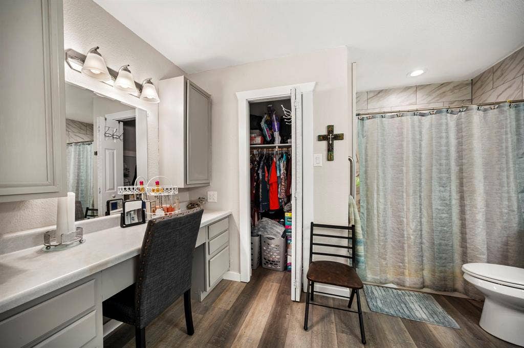 205 Newman Road, Ennis, TX 75119 Bathroom featuring wood-finish flooring, built-in vanity with cabinetry, vanity mirror with overhead lighting, closet, and a shower with tiled surround