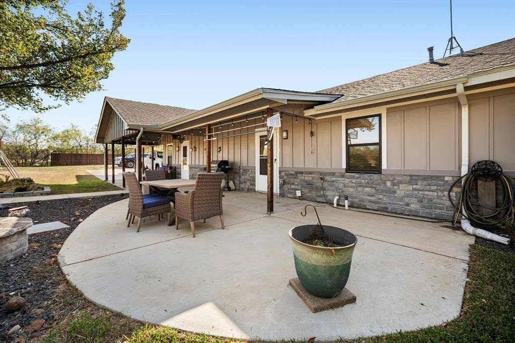 205 Newman Road, Ennis, TX 75119 Covered concrete patio featuring vertical siding, stone veneer accents, and an attached carport