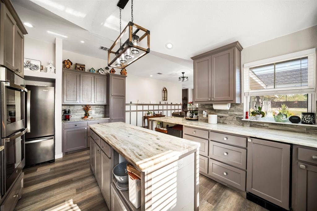 205 Newman Road, Ennis, TX 75119 Kitchen featuring grey shaker-style cabinetry, stone-finish countertops, stone tile backsplash, wood-finish flooring, and a rectangular pendant light fixture