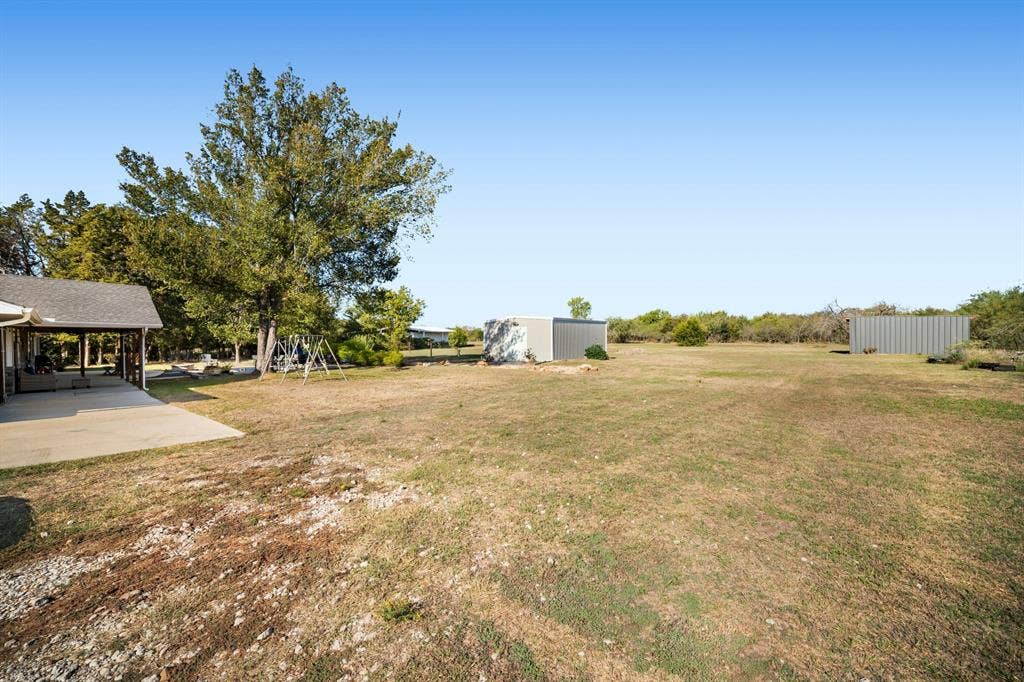 205 Newman Road, Ennis, TX 75119 Expansive grounds featuring a concrete patio, mature trees, two exterior storage buildings, and natural landscape
