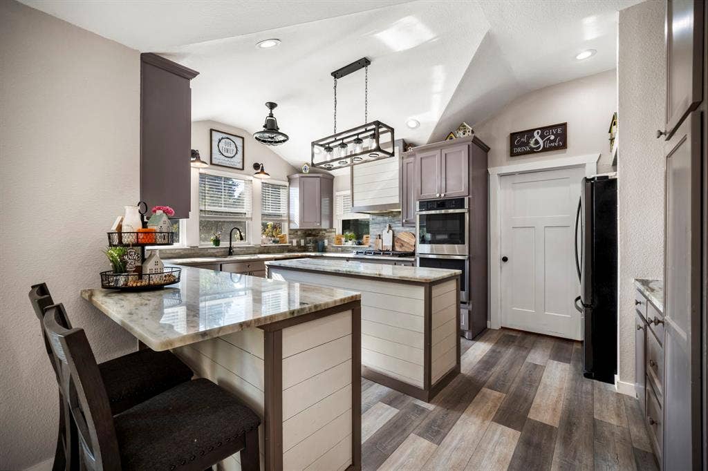 205 Newman Road, Ennis, TX 75119 Kitchen featuring shiplap-accented islands, stone-finish countertops, wood-finish flooring, built-in double ovens, and decorative pendant lighting