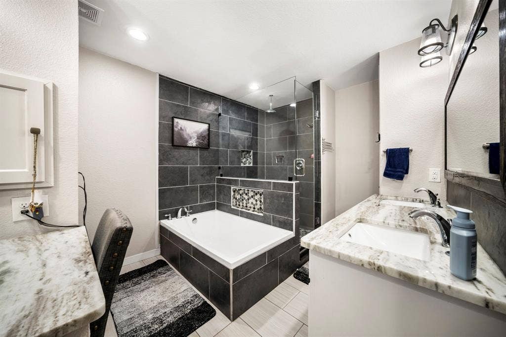 205 Newman Road, Ennis, TX 75119 Dual-sink vanity with stone countertop, soaking tub with tile surround, glass-enclosed shower, and recessed lighting