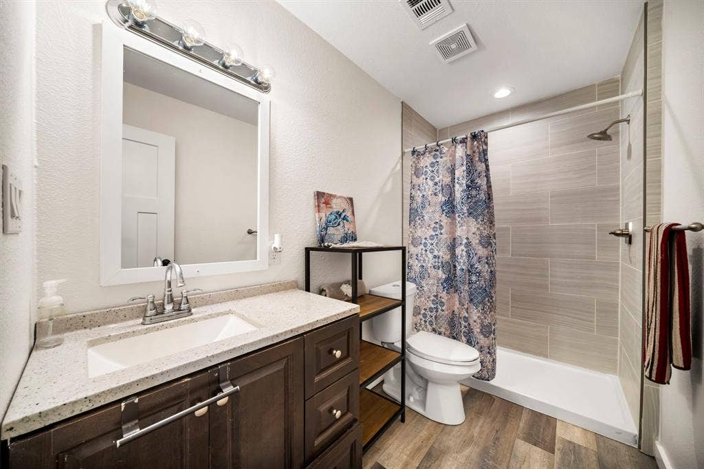 205 Newman Road, Ennis, TX 75119 Bathroom featuring a vanity with a light-toned countertop, framed wall mirror, wood-finish flooring, and a walk-in shower with horizontal tile surround