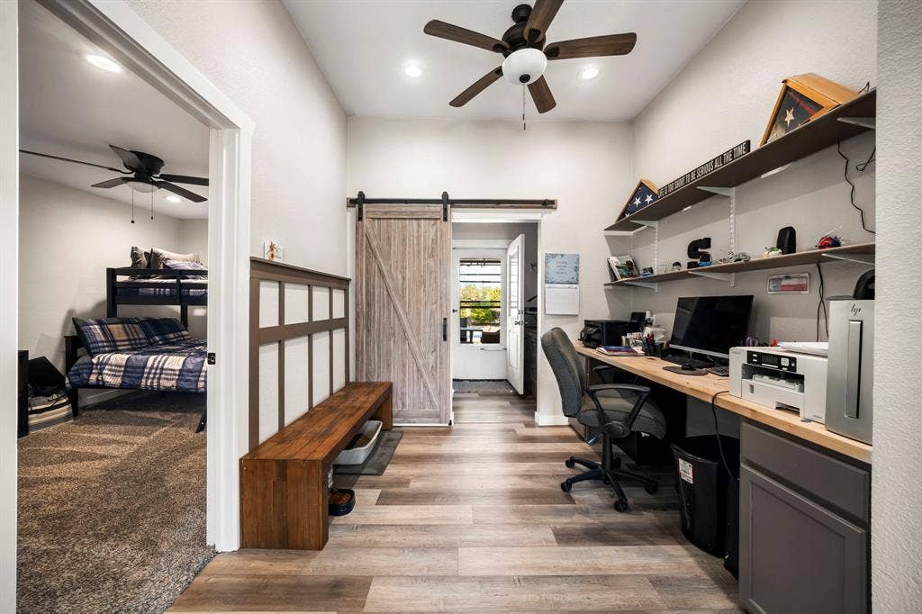 205 Newman Road, Ennis, TX 75119 Interior space featuring wood-finish flooring, a rustic barn-style sliding door, built-in wooden desk cabinetry, wall-mounted shelving, and a decorative wood wainscot panel with a bench